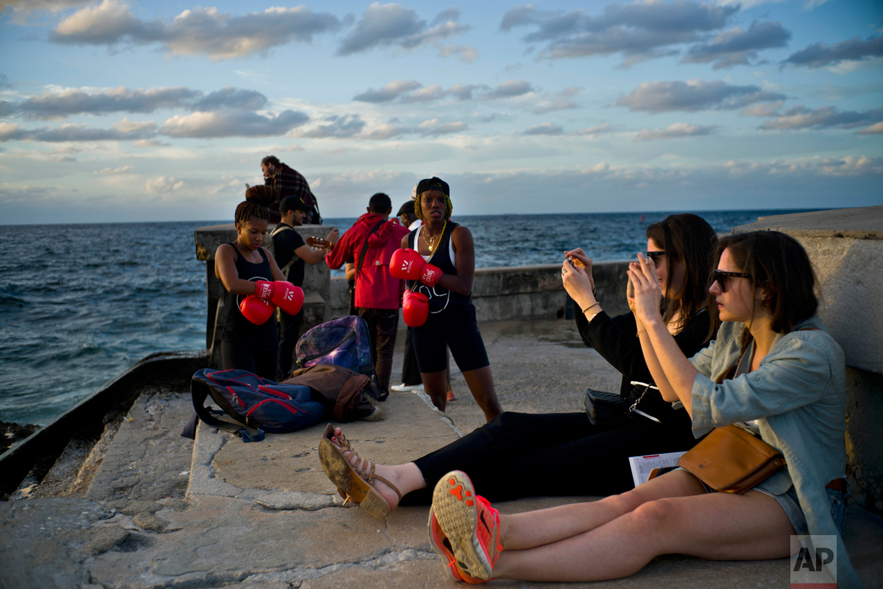 In this Jan. 30, 2017 photo, boxers Idamelys Moreno, left, and Legnis Cala, get ready for a photo session, as tourists take photos of the sunset, on Havana's sea wall in Cuba. Female athletes in Cuba have made strides in many other sports, including wrestling, judo and most recently, weightlifting, but not in boxing. (AP Photo/Ramon Espinosa)