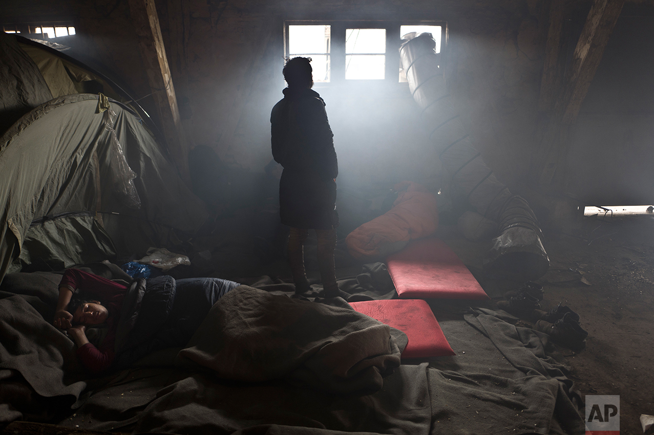  An Afghan refugee man sleeps on the ground while another looks out a window in an abandoned warehouse where they and other migrants took refuge in Belgrade, Serbia, Wednesday, Feb. 1, 2017. (AP Photo/Muhammed Muheisen) 