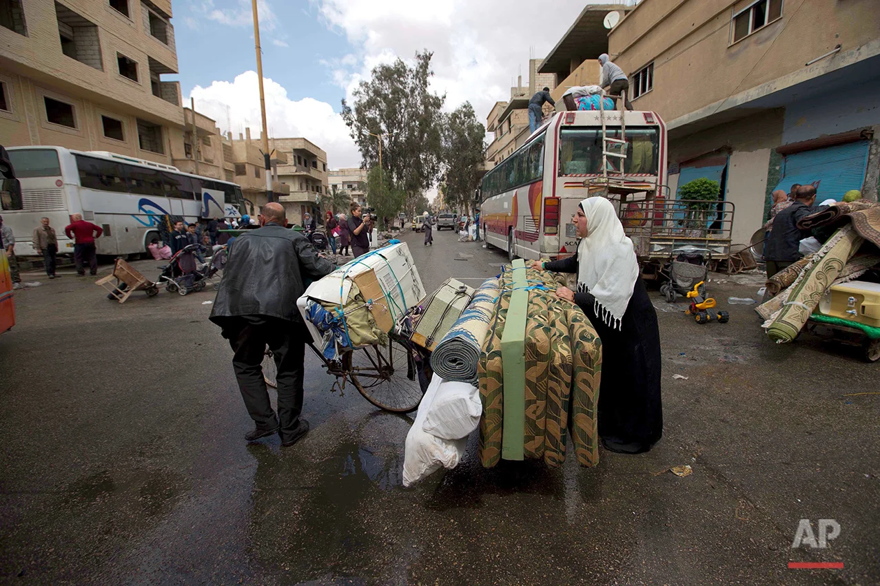 In this picture taken Thursday, April 14, 2016, a Syrian family pulls a bike containing belongings to load them onto a bus in the town of Palmyra in the central Homs province, Syria. (AP Photo/Hassan Ammar)