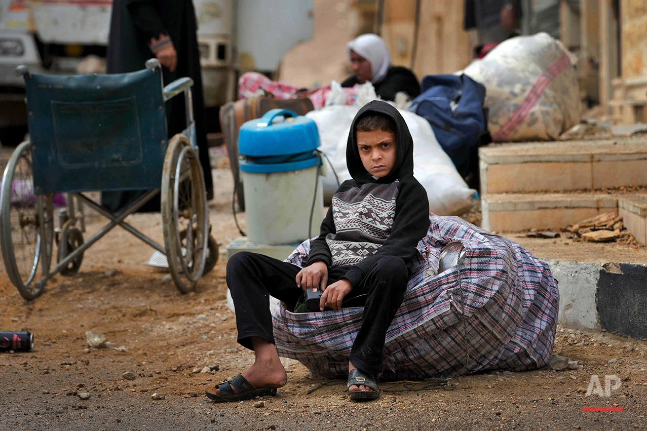 In this picture taken Thursday, April 14, 2016, a Syrian boy waits as his family to loads their belongings onto a bus in the town of Palmyra in the central Homs province, Syria. (AP Photo/Hassan Ammar)