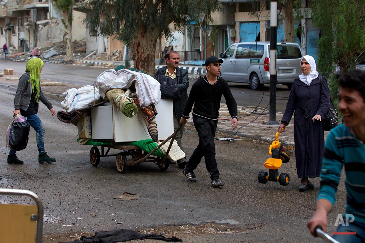 In this picture taken Thursday, April 14, 2016, a Syrian family pulls a trolley containing belongings to load them onto a bus in the town of Palmyra in the central Homs province, Syria. (AP Photo/Hassan Ammar)