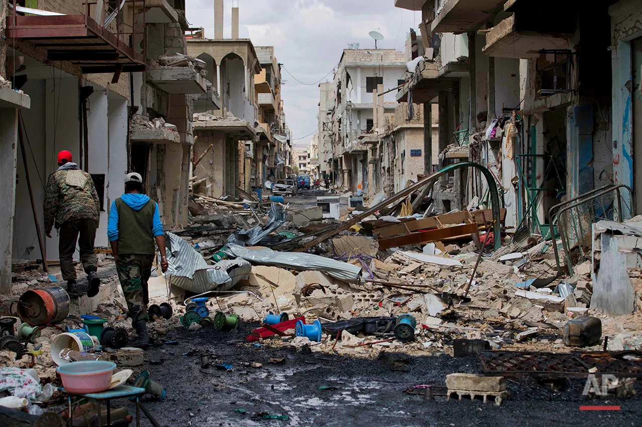 In this picture taken Thursday, April 14, 2016, Syrian soldiers walk through a devastated part of the town of Palmyra as families load their belongings onto a bus in the central Homs province, Syria. (AP Photo/Hassan Ammar)