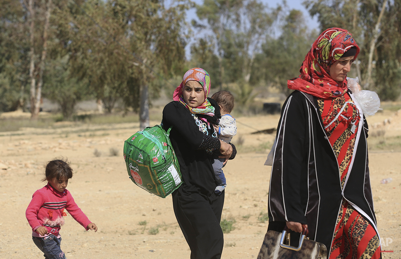 People flee their homes during clashes between Iraqi security forces and Islamic State group in Hit, 85 miles (140 kilometers) west of Baghdad, Iraq, Monday, April 4, 2016. Families, many with small children and elderly relatives say they walked for hours Monday through desert littered with roadside bombs to escape airstrikes and clashes. (AP Photo/Khalid Mohammed)