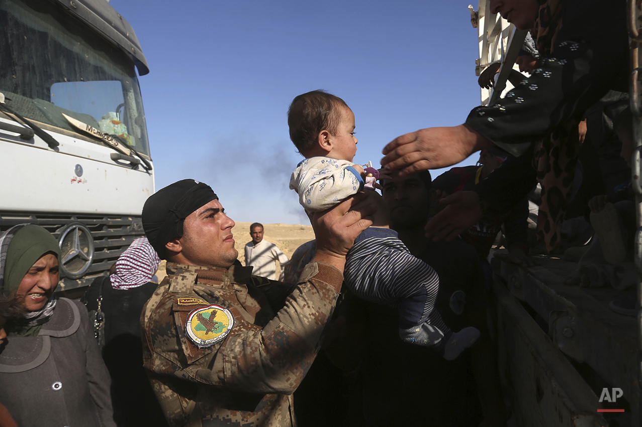 A member of elite counter terrorism forces helps women and children fleeing their homes during clashes between Iraqi security forces and Islamic State group in Hit, 85 miles (140 kilometers) west of Baghdad, Iraq, Monday, April 4, 2016. Families, many with small children and elderly relatives say they walked for hours Monday through desert littered with roadside bombs to escape airstrikes and clashes. (AP Photo/Khalid Mohammed)