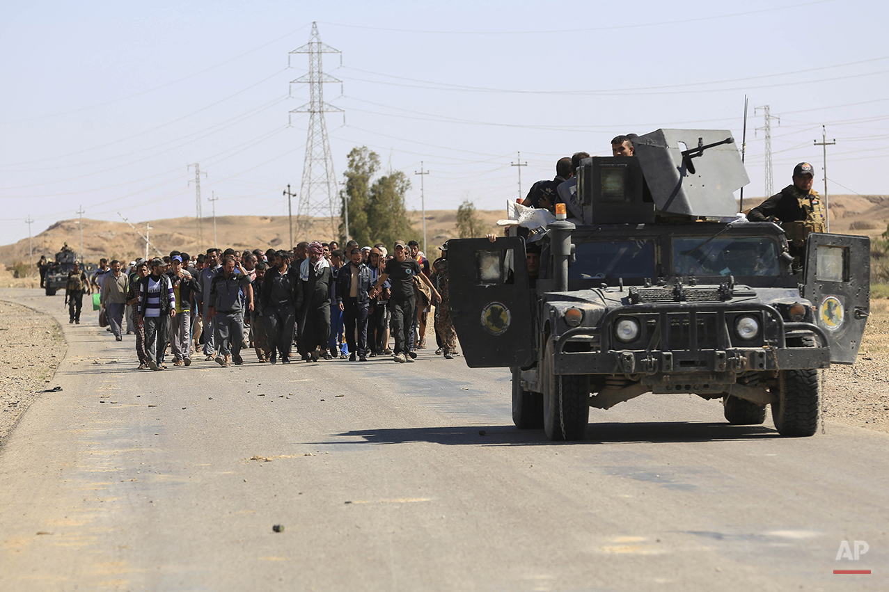Elite counter terrorism forces escort people fleeing their homes during clashes between Iraqi security forces and the Islamic State group in Hit, 85 miles (140 kilometers) west of Baghdad, Iraq, Monday, April 4, 2016. Families, many with small children and elderly relatives say they walked for hours Monday through desert littered with roadside bombs to escape airstrikes and clashes. (AP Photo/Khalid Mohammed)