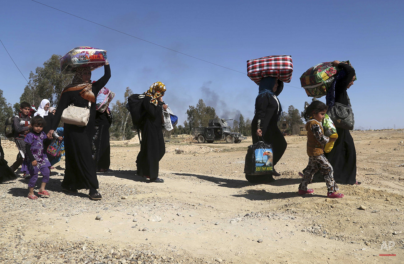People flee their homes during clashes between Iraqi security forces and Islamic State group in Hit, 85 miles (140 kilometers) west of Baghdad, Iraq, Monday, April 4, 2016. Families, many with small children and elderly relatives say they walked for hours Monday through desert littered with roadside bombs to escape airstrikes and clashes. (AP Photo/Khalid Mohammed)
