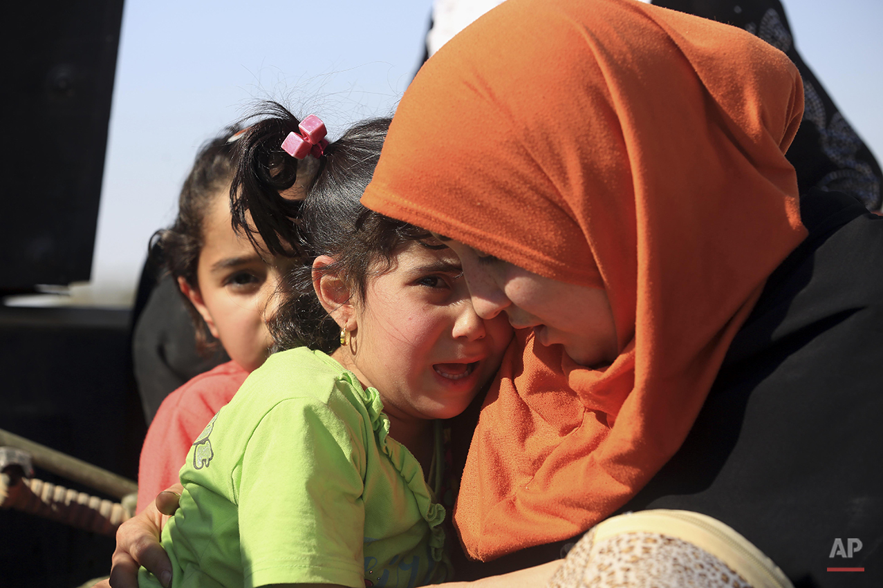 People flee their homes during clashes between Iraqi security forces and Islamic State group in Hit, 85 miles (140 kilometers) west of Baghdad, Iraq, Monday, April 4, 2016. Families, many with small children and elderly relatives say they walked for hours Monday through desert littered with roadside bombs to escape airstrikes and clashes. (AP Photo/Khalid Mohammed)