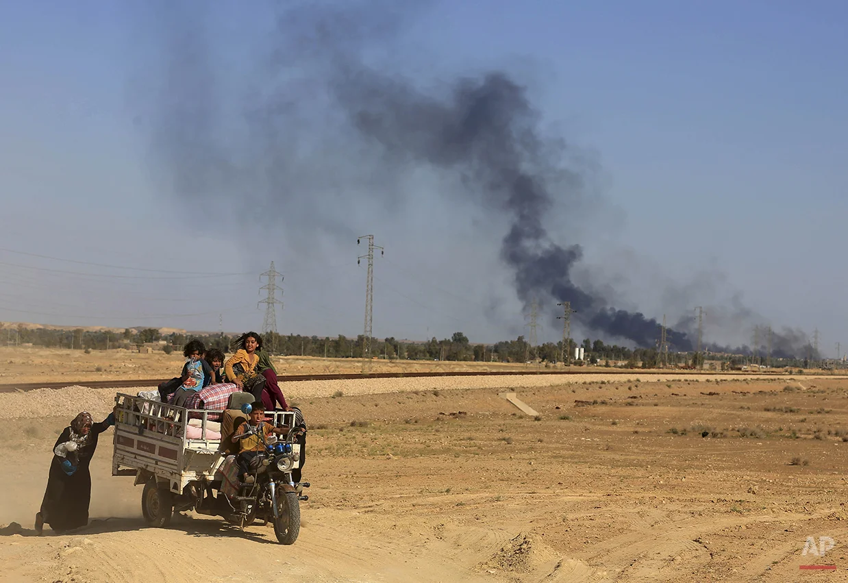 Smoke rises as people flee their homes during clashes between Iraqi security forces and Islamic State group in Hit, 85 miles (140 kilometers) west of Baghdad, Iraq, Monday, April 4, 2016. Families, many with small children and elderly relatives say …