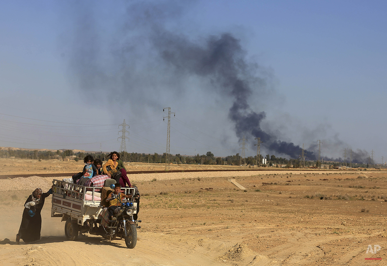 Smoke rises as people flee their homes during clashes between Iraqi security forces and Islamic State group in Hit, 85 miles (140 kilometers) west of Baghdad, Iraq, Monday, April 4, 2016. Families, many with small children and elderly relatives say they walked for hours Monday through desert littered with roadside bombs to escape airstrikes and clashes. (AP Photo/Khalid Mohammed)