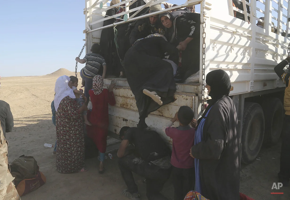 A member of elite counter terrorism forces helps women and children fleeing their homes during clashes between Iraqi security forces and Islamic State group in Hit, 85 miles (140 kilometers) west of Baghdad, Iraq, Monday, April 4, 2016. Families, many with small children and elderly relatives say they walked for hours Monday through desert littered with roadside bombs to escape airstrikes and clashes. (AP Photo/Khalid Mohammed)