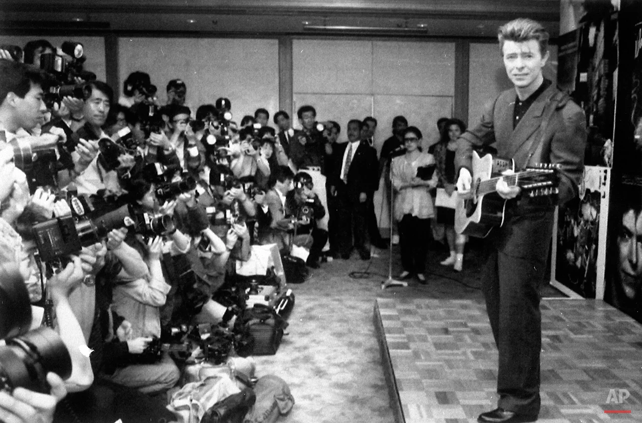 David Bowie plays an acoustic guitar while being photographed at a press conference in Japan on May 19, 1990. (AP Photo)