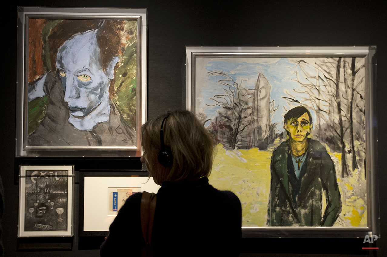 A woman looks at paintings by deceased popstar David Bowie, the one at right of popstar Iggy Pop, at the Groninger Museum which hosts the "DAVID BOWIE is' exhibit, in Groningen, northern Netherlands, Monday, Jan. 11, 2016. The museum is normally closed on Mondays but opened its doors to allow people to sign a condolence register and visit the Bowie exhibit which runs till March 13, 2016. (AP Photo/Peter Dejong)