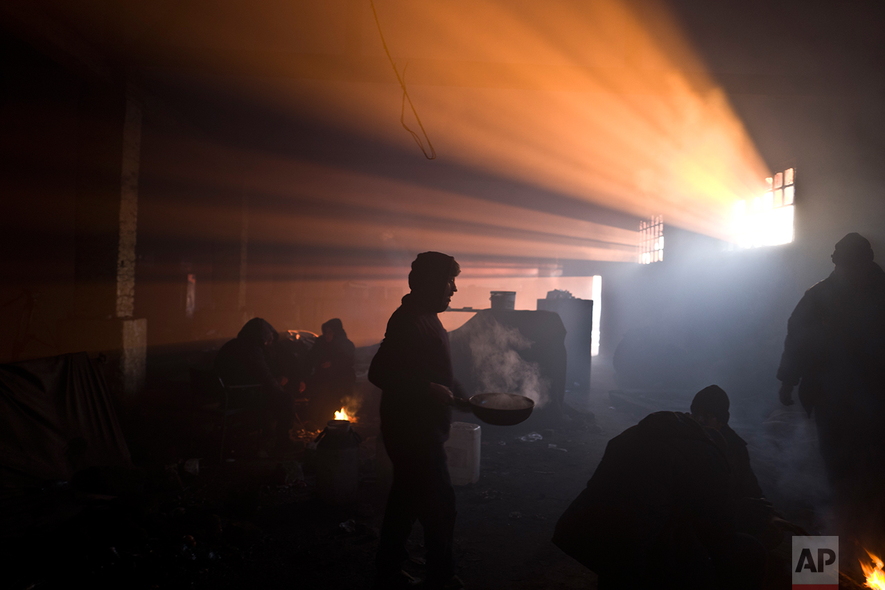  An Afghan refugee man carries a pan while other migrants gather around a fire in an abandoned warehouse in Belgrade, Serbia, Monday, Jan. 30, 2017. (AP Photo/Muhammed Muheisen) 