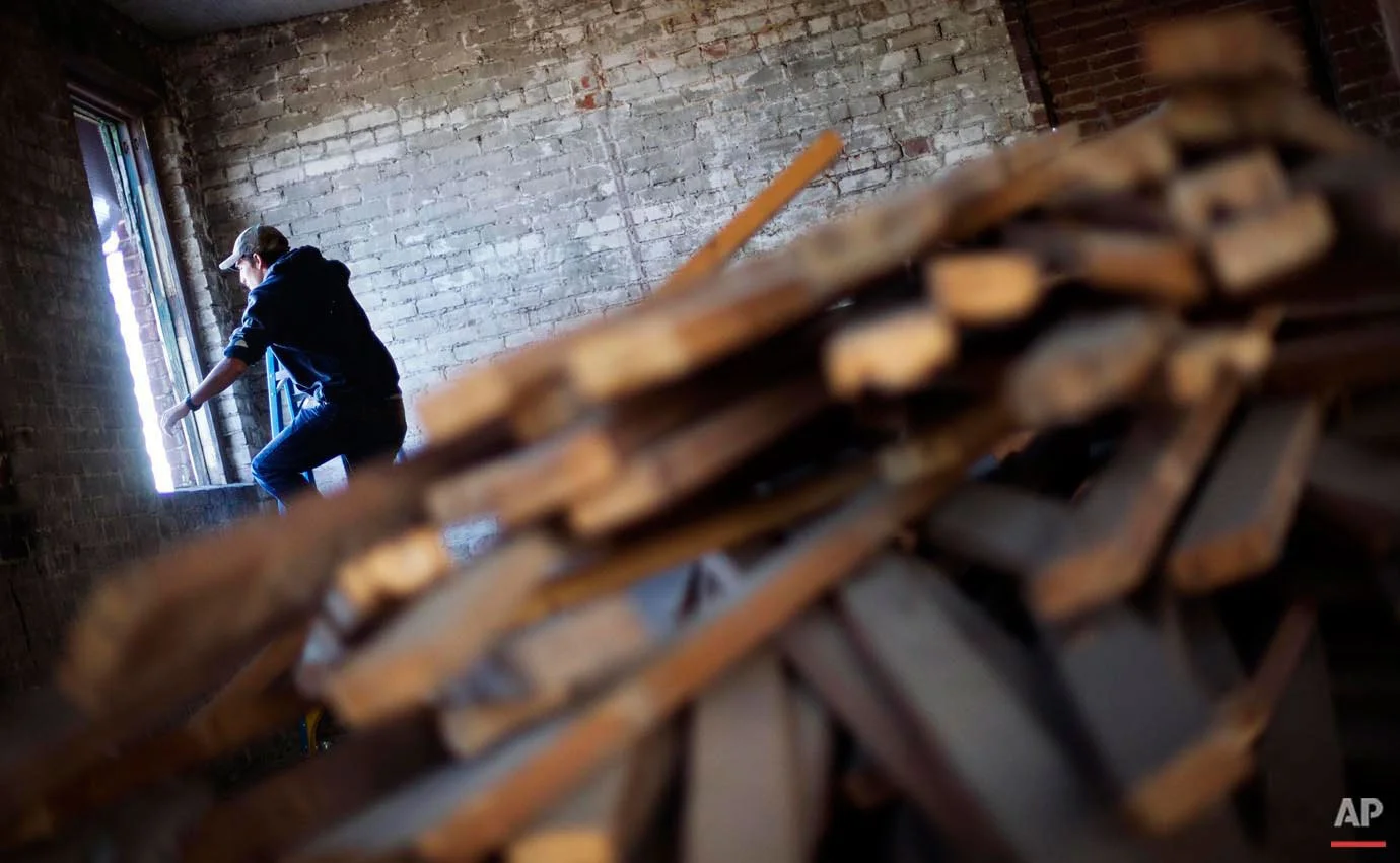 Reclaimed wood sits in the foreground as Glen Wilson, 22, crawls onto the roof of the Coalfield Development Corp. for a class on installing solar panels Monday, Oct. 5, 2015, in Huntington, W.Va. The program hires graduates of high school vocational programs to restore, repurpose or tear down old buildings, use old building materials to make furniture, or build new homes on reclaimed coalfield land. Employees also are also required to take six hours of community college courses a week and three hours of life skills classes that help them with things like money management and healthy eating. (AP Photo/David Goldman)