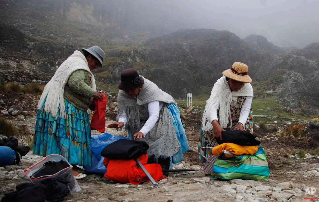 In this Dec. 16, 2015 photo, Aymara indigenous women, from right, Pacesa Alana Llusco, Dora Magueno Machaca and Bertha Vetia prepare their backpacks as they prepare to hike up the Huayna Potosi mountain on the outskirts of El Alto, Bolivia. Not letting their traditional, long multi-layered skirts get in the way, they put on their mountain gear and climbed one of the highest mountains in the country. (AP Photo/Juan Karita)