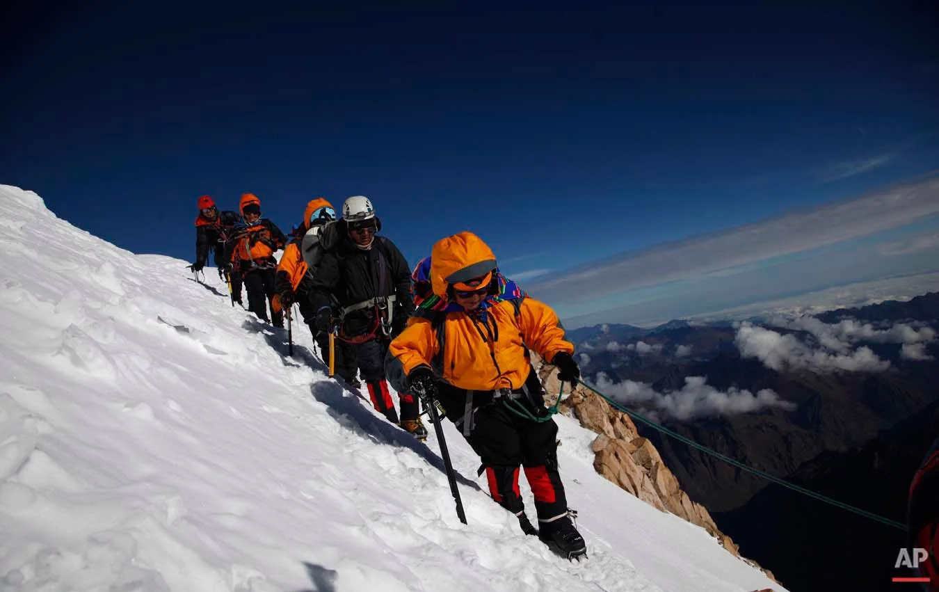 In this Dec. 17, 2015 photo, Aymara indigenous women walk with their guide as they descend the snow capped Huayna Potosi mountain on the outskirts of El Alto, Bolivia. Eleven Aymara women, ranging in age from 20 to 50 years old, made the two-day climb up the mountain. All of the women work as porters and cooks at the base camp, but six of the youngest ones would like to eventually join the ranks of the men and guide tourists to the peak. (AP Photo/Juan Karita)