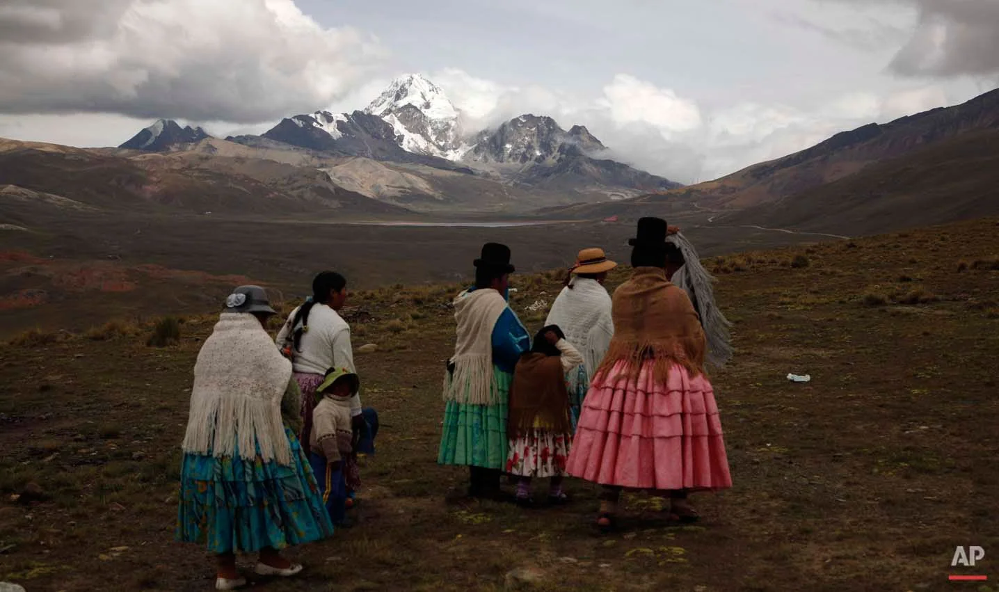 In this Dec. 16, 2015 photo, Aymara indigenous women look at the Huayna Potosi mountain before climbing it on the outskirts of El Alto, Bolivia. At first glance, the women known as "cholitas" don’t look much like mountain climbers, with their colorful, multilayered skirts and fringed shawls, but they've been climbing for 15 years, cooking and carrying food for tourists who climb to the peak. (AP Photo/Juan Karita)