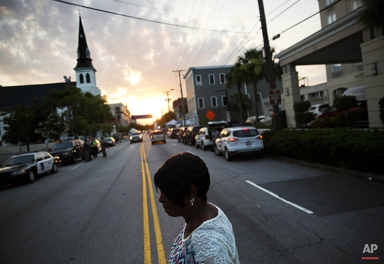 A woman crosses the street on her way to visit a sidewalk memorial to the Emanuel AME Church shooting victims as the sun rises next to the church's steeple Sunday, June 21, 2015, in Charleston, S.C. Congregation members say the historic black church where nine people were killed is going to re-open for Sunday morning service. (AP Photo/David Goldman)