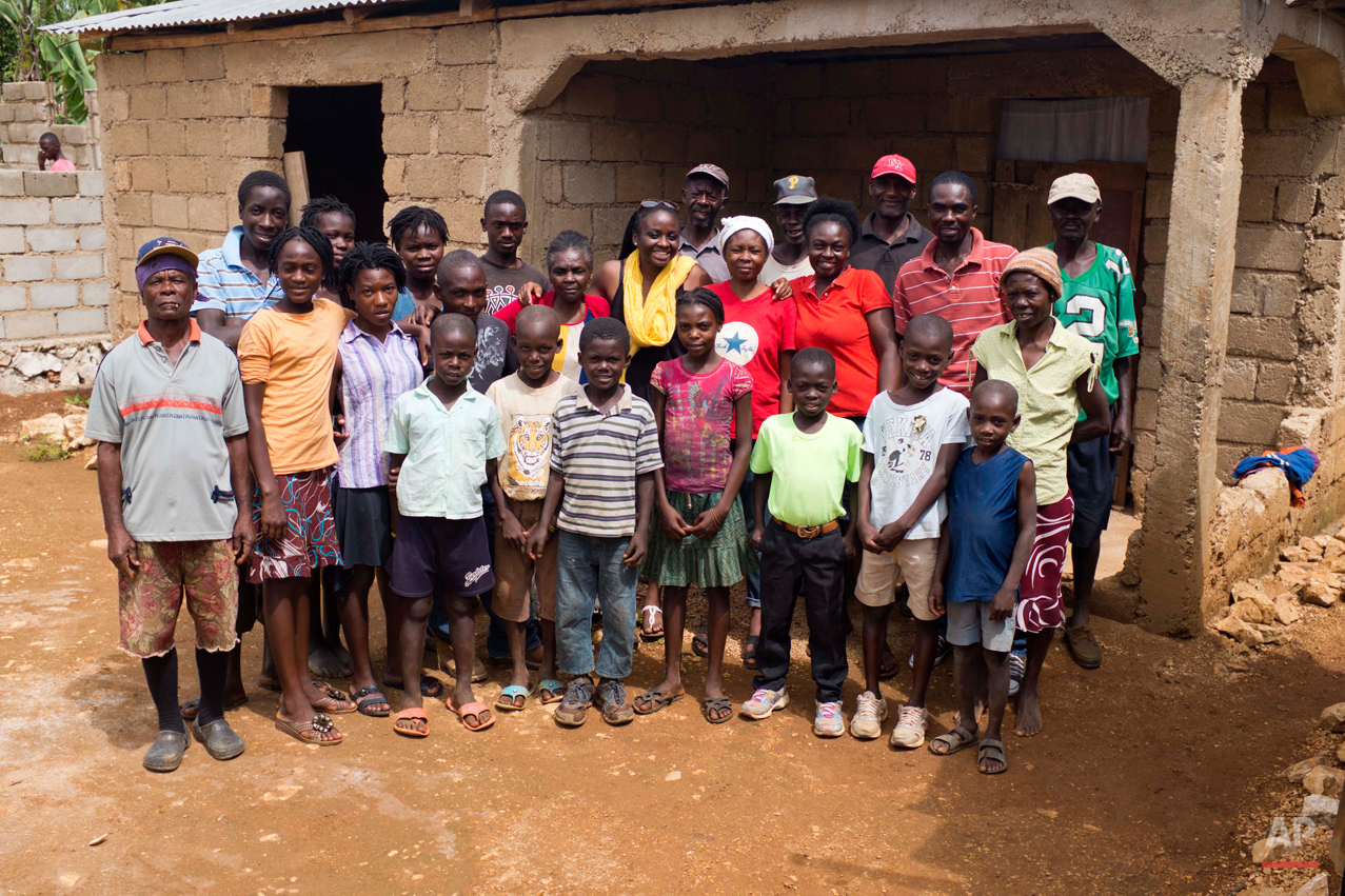  In this July 14, 2015 photo, Mariette Williams, wearing a yellow scarf, poses for a group photo with her newfound relatives outside their home in Deron, a neighborhood on the outskirts of Pestel, Haiti. A Florida teacher with a master's degree, Mari