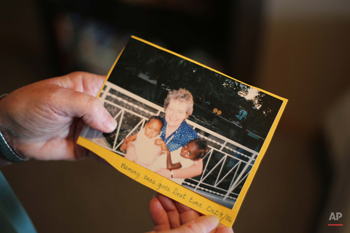  In this Nov. 6, 2015 photo, adoptive mother Sandra Knopf holds a picture of herself and the two Haitian children, Patricia, left, and Mariette, right, she adopted from a Port-au-Prince orphanage, at her home in Armstrong, British Columbia, Canada.  