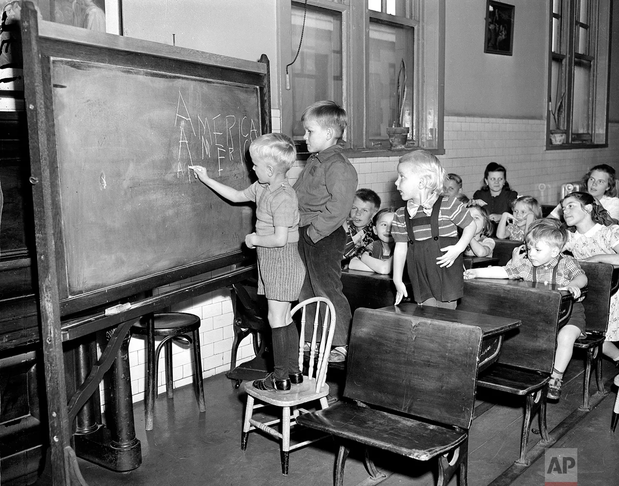 In this April 7, 1949 photo, three Finnish children write "America" on a chalkboard in a class held for children of immigrants detained at Ellis Island in New York City. They range in ages 3 to 11 years old. The American self-image is forever intertwined with the melting pot _ a nation that embraces the world’s wretched refuse, a nation built by immigrants. But America’s immigration history is complicated. (AP Photo)