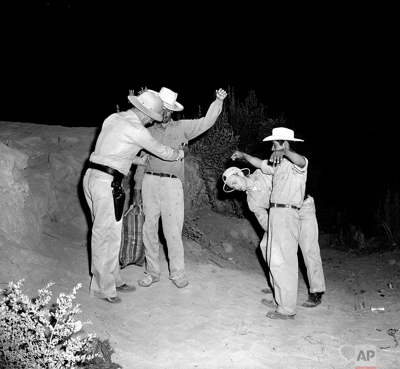 In this Aug. 11, 1951 photo, U.S. Border Patrol inspectors Fred H. Voight, left, and Gordon MacDonald, right, both from the El Centro U.S. Border Patrol sector headquarters, search two Mexican nationals, Pedro Vidal, with bag, and Canuto Garcia, right, shortly after the two men illegally crossed the border from Mexico, west of Calexico, Calif. Mexican laborers try to cross in this area to the United States, to work on the farms of the nearby Imperial Valley. (AP Photo)