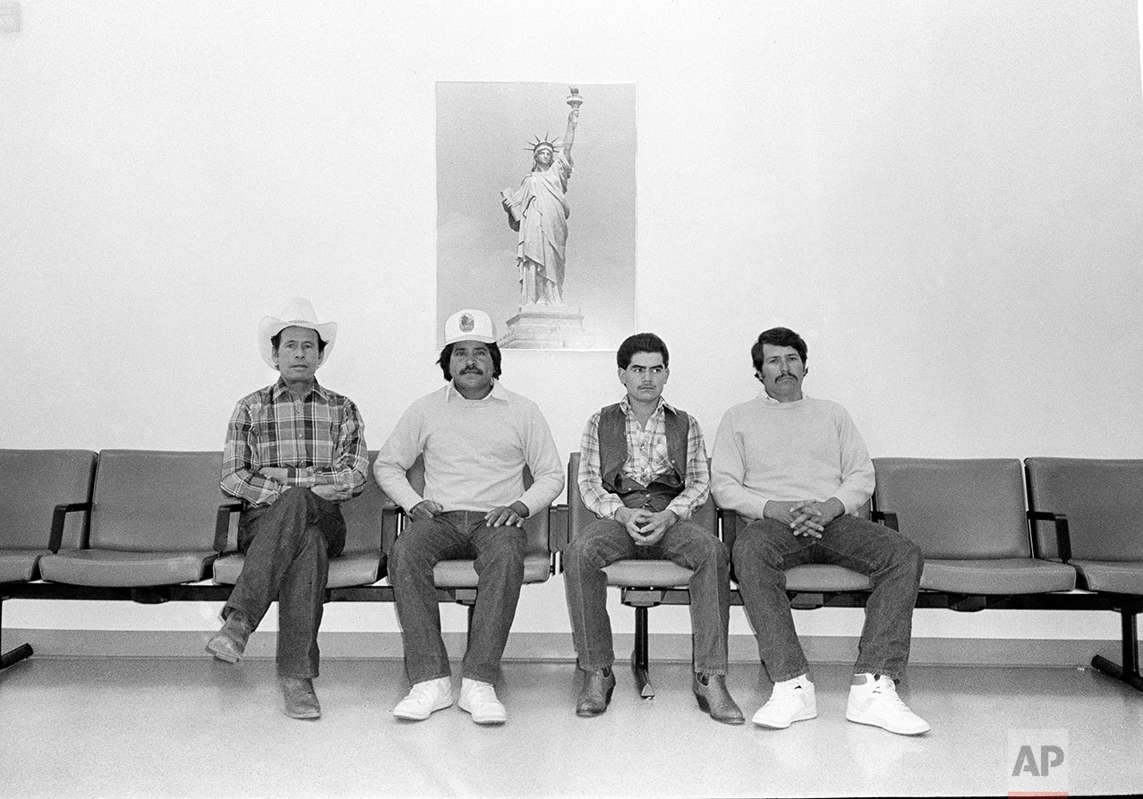 Alejandro Fierro, right, and three other Mexican farm workers sit under a poster of the Statue of Liberty at the U.S. Immigration and Naturalization Service office in Denver, Colo., Nov. 11, 1987. Fierro and the others were waiting to begin the application process for amnesty under the landmark Immigration Control and Reform Act of 1986. From left are: Jose Duenas-Lopez; Jose Santillano; Carlo Castro-Gutierres and Fierro. (AP Photo)