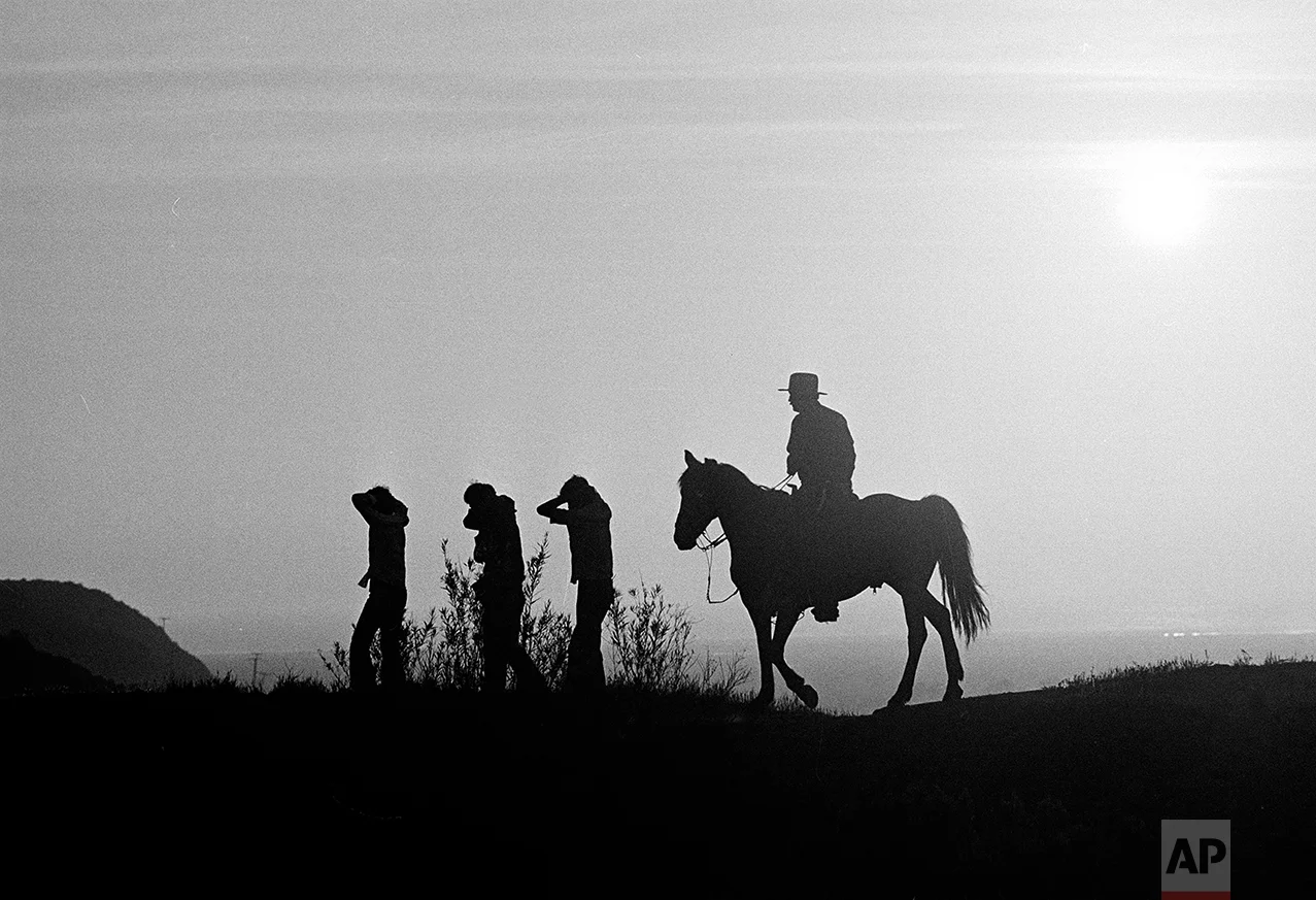 U.S. Border Patrol officer Ed Pyeatt, on horseback, leads a group of illegal aliens down the hillside toward waiting vans for the trip to a holding center at the Chula Vista border station. According to Pyeatt, a monthly average of 10, 000 illegals are captured in this 6-mile stretch of border, Aug. 18, 1981. (AP Photo)