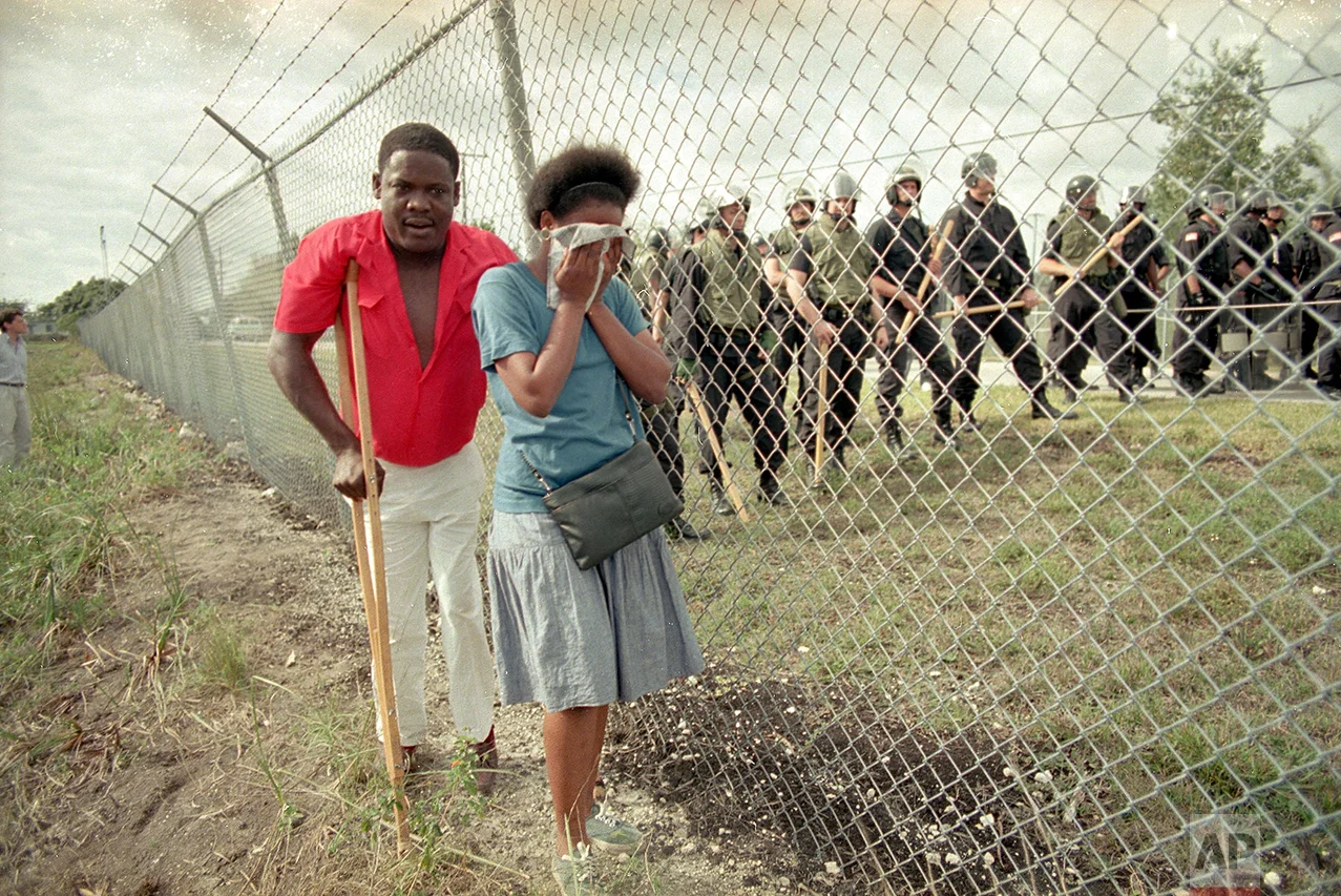 Paula Vivaldy cries as she and friend Bilatois Thermidor walk beside the barbed wire fence at the U.S. Immigration Service's Krome Avenue Detention Center, in Miami, where some 200 Haitians gathered to protest the treatment of Haitians held there, Jan. 29, 1989. Inside the fence several dozen federal officers in riot gear stand at the ready for any trouble. (AP Photo/Kathy Willens)