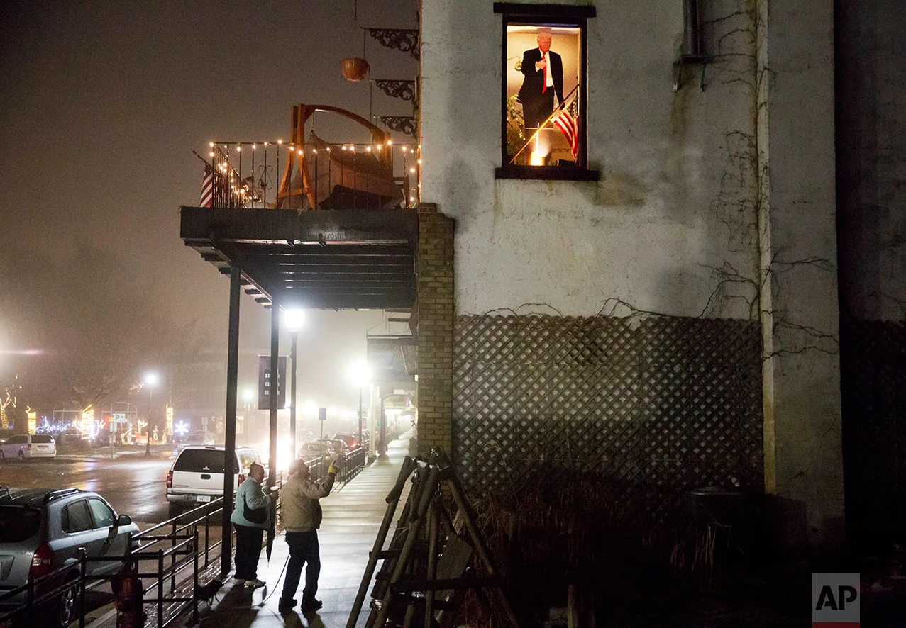 A cardboard cutout of President Donald Trump sits in a window as pedestrians notice it from below in McGregor, Iowa, Friday, Jan. 20, 2017. Some 50 counties stretching 300 miles down the Mississippi River, through Minnesota, Wisconsin, Iowa and Illinois, switched from blue to red in November. (AP Photo/David Goldman)