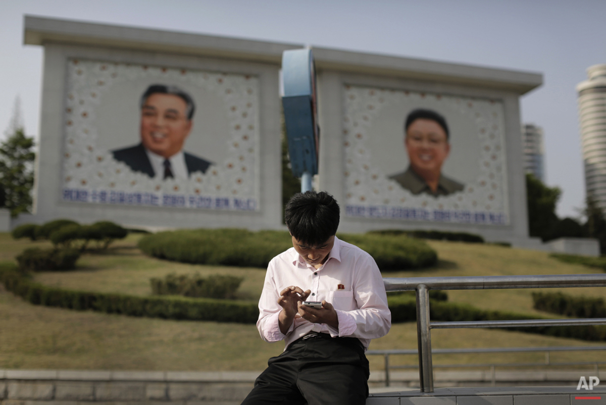  In this Tuesday, May 5, 2015, photo, a man sits in front of portraits of the late North Korean leaders Kim Il Sung, left, and Kim Jong Il, right, as he uses his smartphone in Pyongyang, North Korea. North Korean officials have unveiled a mobile-frie
