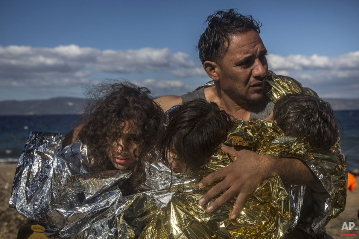  A man holds three children wearing thermal blankets after their arrival in bad weather from Turkey on the Greek island of Lesbos , Wednesday, Oct. 28, 2015. (AP Photo/Santi Palacios) 