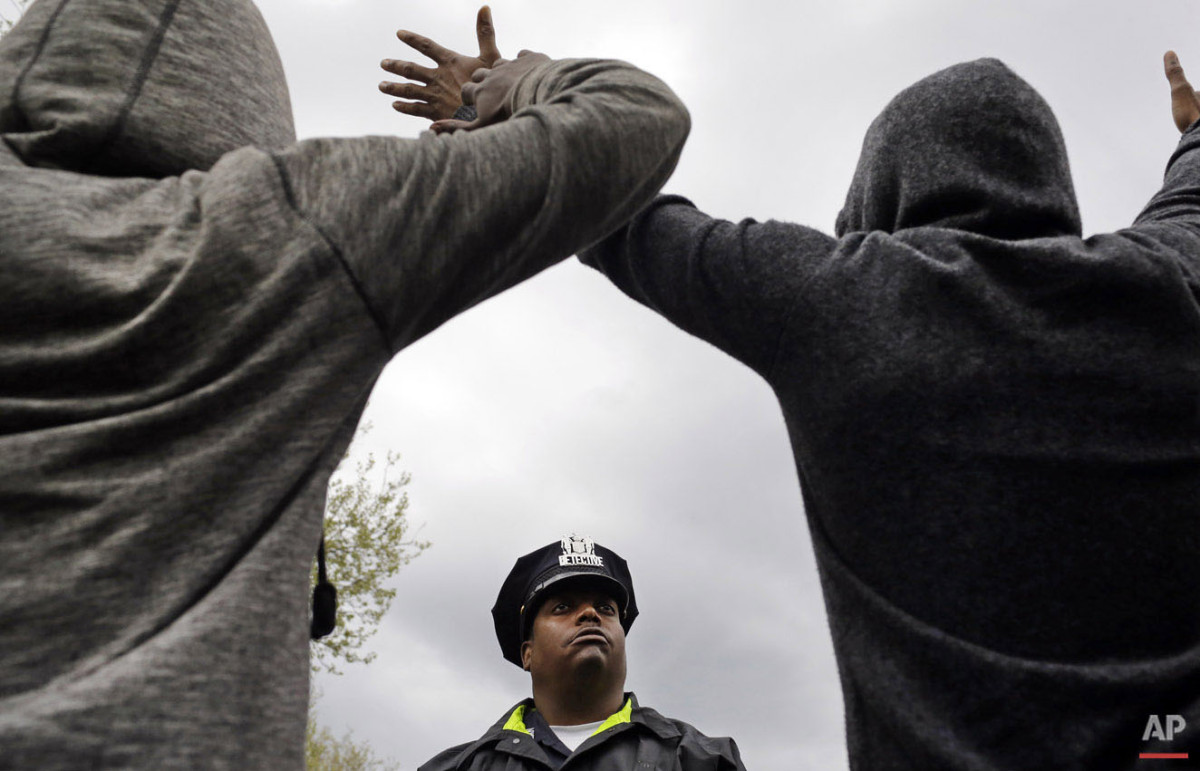  A member of the Baltimore Police Department stands guard outside of the department's Western District police station as men hold their hands up in protest during march for Freddie Gray, Wednesday, April 22, 2015, in Baltimore. (AP Photo/Patrick Sema