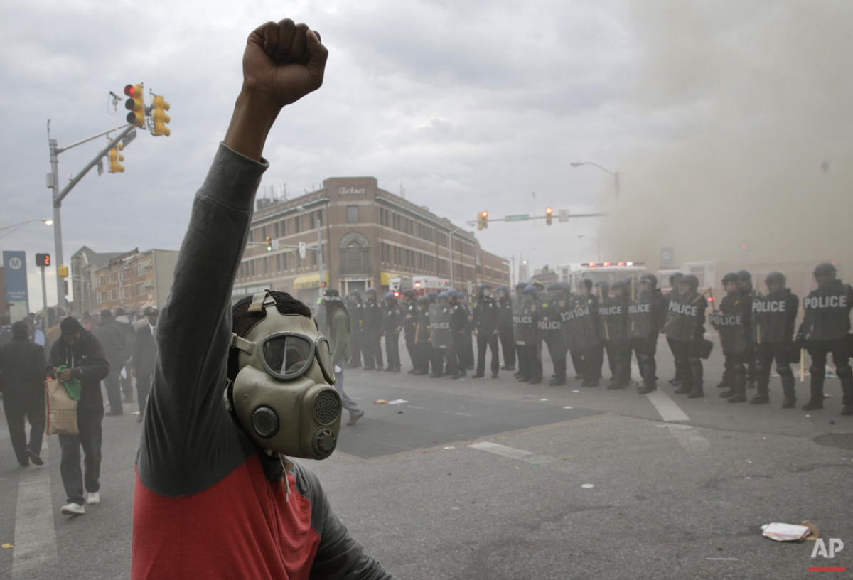  A demonstrator raises his fist as police stand in formation and a CVS store burns, Monday, April 27, 2015, during unrest following the funeral of Freddie Gray in Baltimore. (AP Photo/Patrick Semansky) 