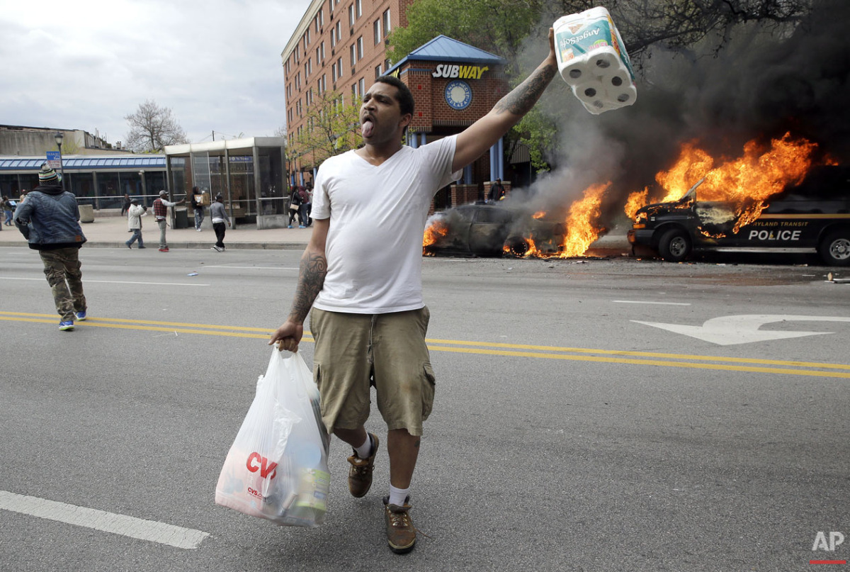  A man carries items that he looted from a store as police vehicles burn, Monday, April 27, 2015, after the funeral of Freddie Gray in Baltimore. (AP Photo/Patrick Semansky) 