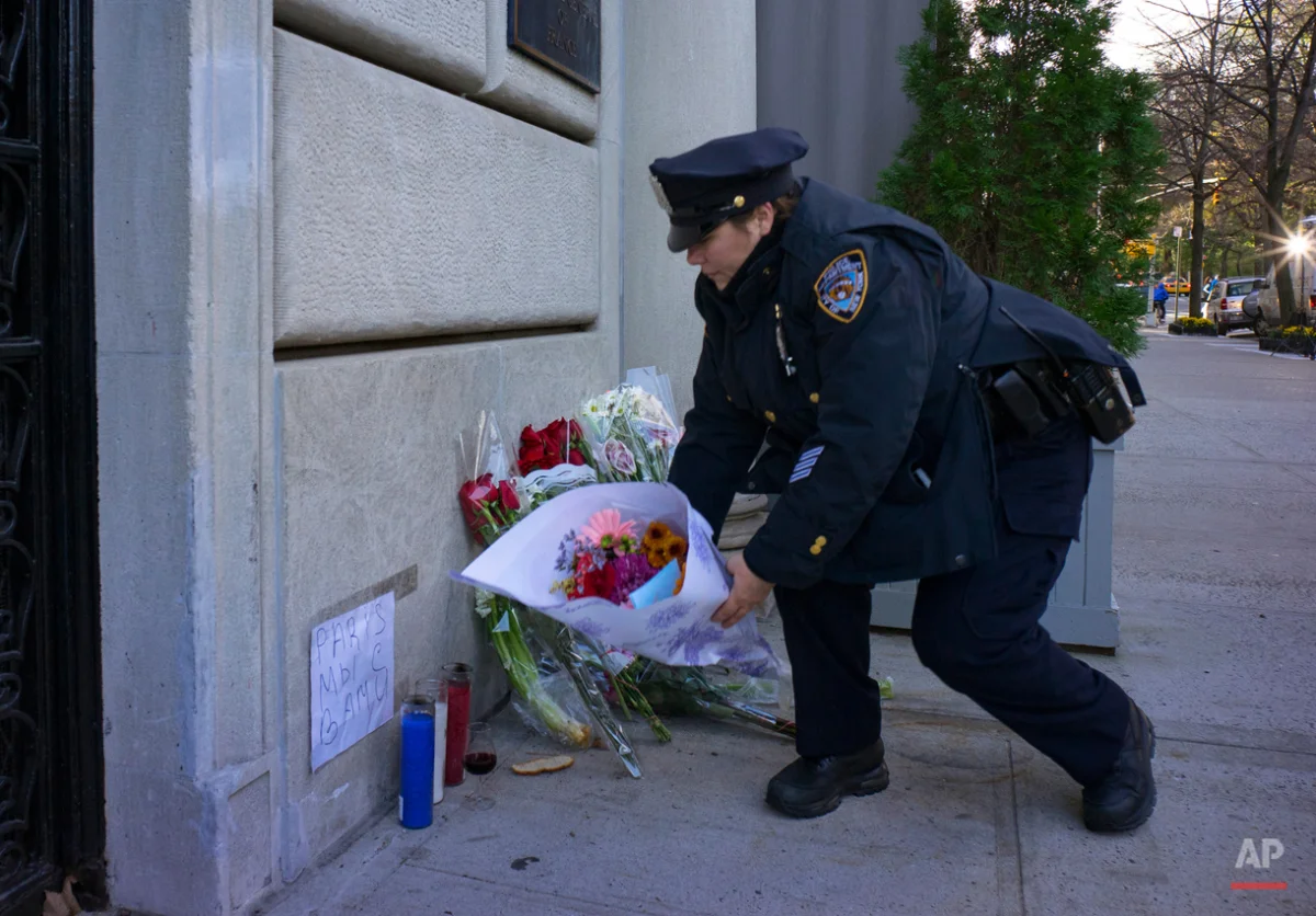 A New York City police officer adjusts wind blown flowers left as a sign of support to France near the door of the French consulate in New York, Saturday, Nov. 14, 2015. Multiple attacks across Paris on Friday night have left scores dead and hundreds injured.(AP Photo/Craig Ruttle)