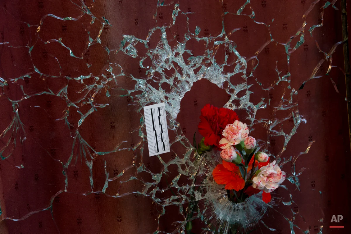Flowers are put in a window shattered by a bullet as a forensic marker sits next to the impact as people pay their respect to the victims at the site of the attacks on restaurant Le Petit Cambodge (Little Cambodia) and the Carillon Hotel on the first of three days of national mourning in Paris, Sunday, Nov. 15, 2015. Thousands of French troops deployed around Paris on Sunday and tourist sites stood shuttered in one of the most visited cities on Earth while investigators questioned the relatives of a suspected suicide bomber involved in the country's deadliest violence since World War II. (AP Photo/Peter Dejong)