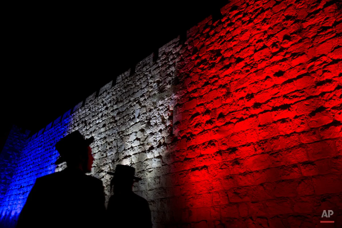 Two Ultra-Orthodox Jews look at Jerusalem's Old City walls illuminated by the colors of the French national flag in solidarity with France after attacks in Paris, in Jerusalem, Sunday, Nov. 15, 2015. (AP Photo/Ariel Schalit)