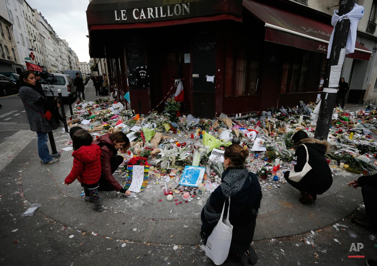 People lay flowers and candles in front of the restaurant Le Carillon, one of the establishments targeted in Friday's gun and bomb attacks, in Paris, Monday, Nov. 16, 2015. French police raided more than 150 locations overnight as authorities released the names of two more potential suicide bombers involved in the Paris attacksó one born in Syria, the other a Frenchman wanted as part of a terrorism investigation. (AP Photo/Frank Augstein)