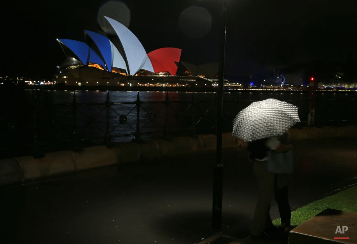 A couple look at the sails of the Sydney Opera House that are lit in the colors of the French flag in Sydney, Saturday, Nov. 14, 2015, following the terrorist attacks in Paris. French police are hunting for possible accomplices of assailants who terrorized Paris concert-goers, cafe diners and soccer fans in the countryÌs deadliest peacetime attacks, a succession of explosions and shootings that cast a dark shadow over this luminous tourist destination. (AP Photo/Rick Rycroft)