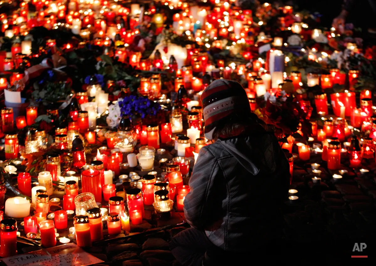 A young girl sits next to flowers and candles placed outside the French embassy in Prague, Czech Republic, Saturday, Nov. 14, 2015, after the attacks in Paris on Friday. French officials said scores of people died Friday night when attackers launched gun attacks at Paris cafes, detonated suicide bombs near France's national stadium and killed hostages inside a concert hall during a rock show. (AP Photo/Petr David Josek)