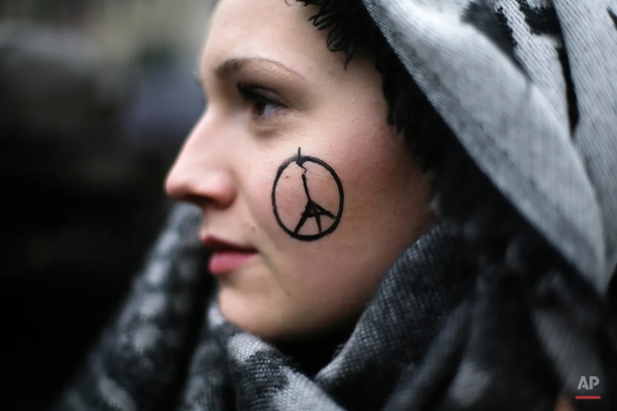 A woman has a peace sign combined with the Eiffel Tower painted on her face as she arrives for a minute of silence for the victims of Friday's attacks in Paris, in front of the French Embassy in Berlin, Sunday, Nov. 15, 2015. Multiple attacks across Paris on Friday night have left scores dead and hundreds injured. (AP Photo/Markus Schreiber)