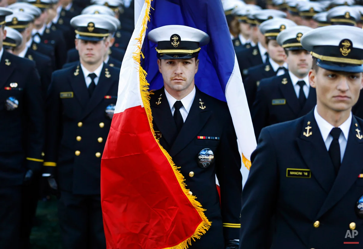 A U.S. Naval Academy midshipman is enveloped by the French national flag as it is caught in a gust of wind before an NCAA college football game between Navy and SMU, Saturday, Nov. 14, 2015, in Annapolis, Md. The brigade of midshipmen marched onto the field with the flag in response to attacks in Paris. (AP Photo/Patrick Semansky)