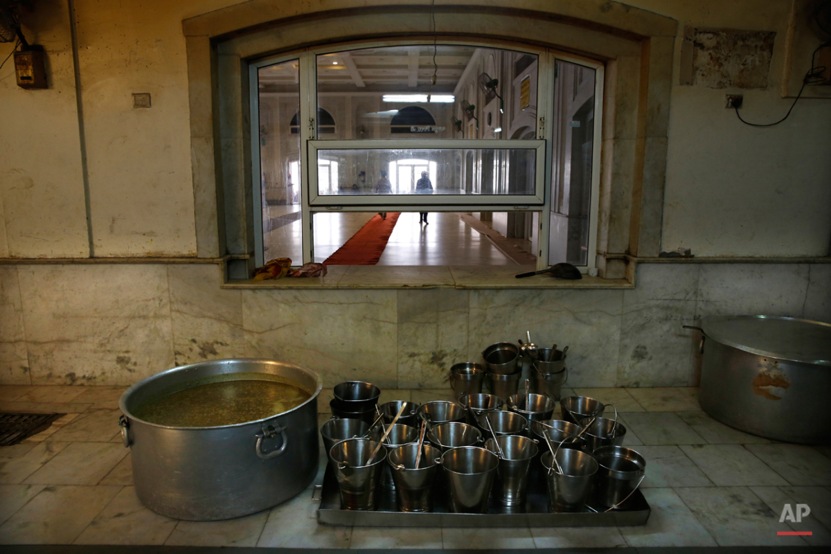  In this May 12, 2015 photo, empty buckets are placed next to a large tub of lentils before the start of langar, which translates to community dinner, at the Bangla Sahib Gurdwara or Sikh temple, in New Delhi, India. Men, women and children throng th