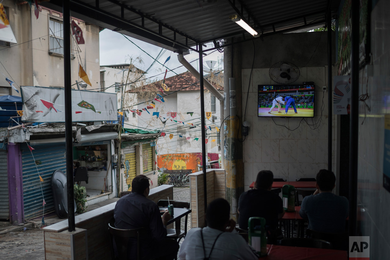  People watch on a television the men's judo competition at at the 2016 Summer Olympics as they sit for lunch at the Dona Marta slum in Rio de Janeiro, Brazil, Wednesday, Aug. 10, 2016. (AP Photo/Felipe Dana) 