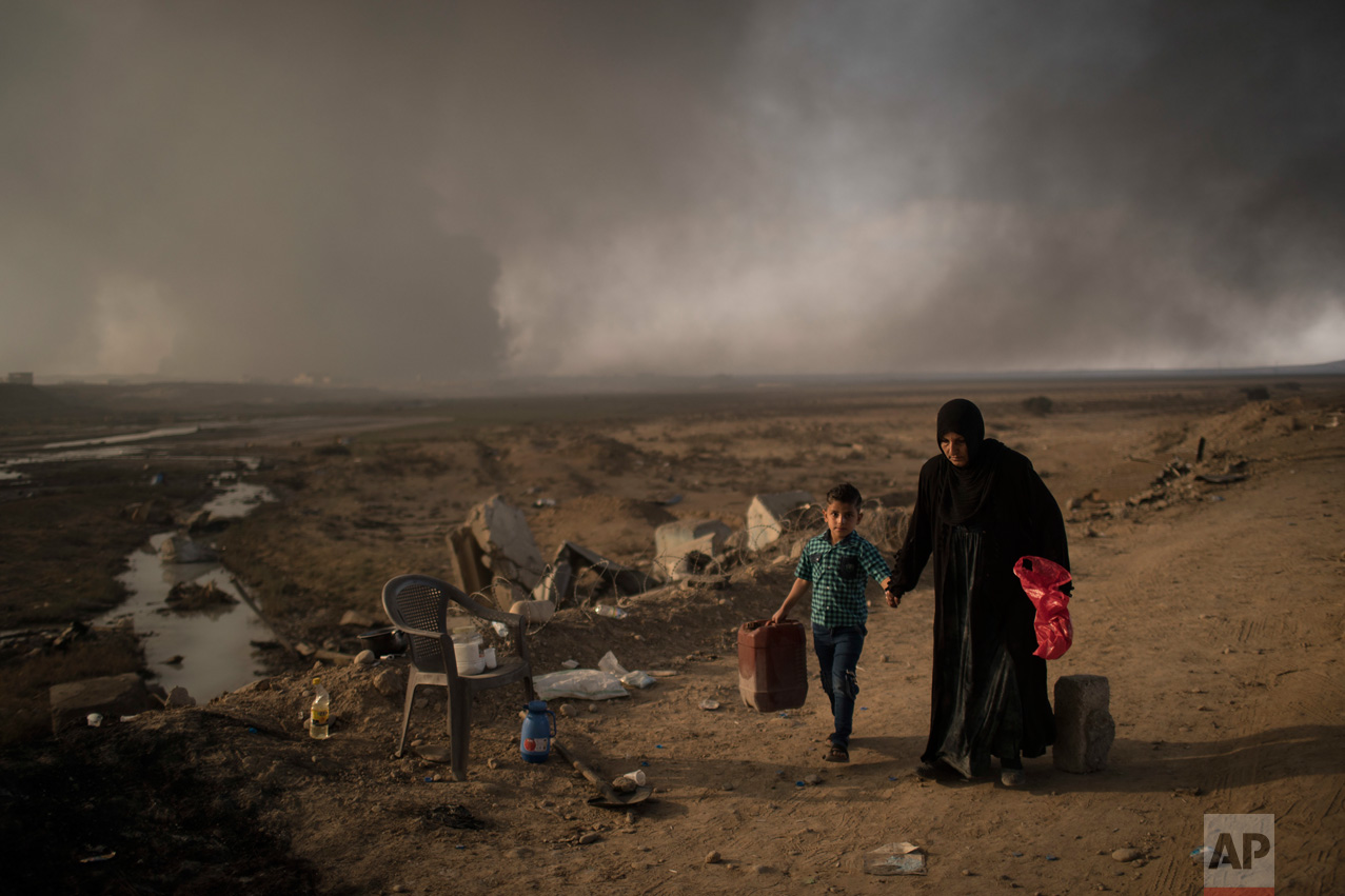  In this Sunday, Nov. 6, 2016 photo, displaced people walk past a checkpoint near Qayara, south of Mosul, Iraq. As the operation to retake Mosul enters its second month Iraqi forces are preparing for prolonged, grueling urban combat as they slow the 