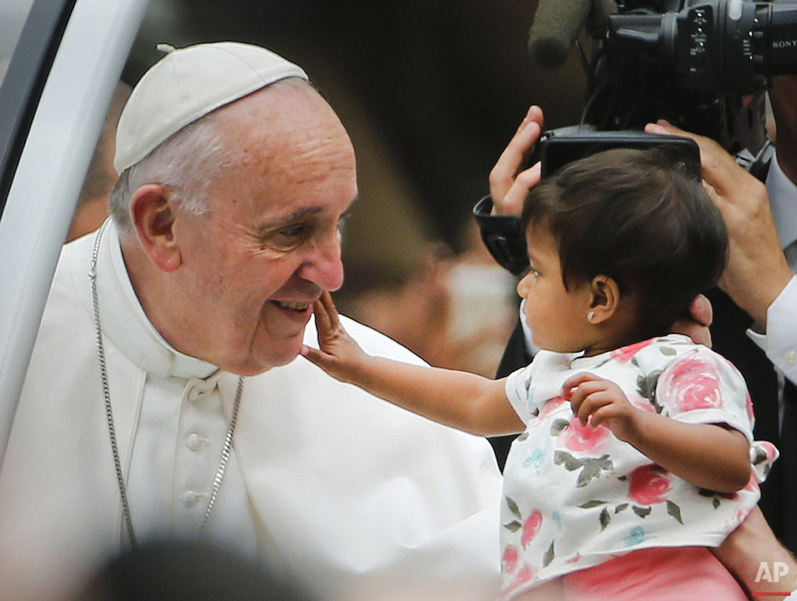  An unidentified child, who was carried out from the crowd to meet Pope Francis, reaches out to touch the Pontiff's face during a parade on his way to celebrate Sunday Mass on the Benjamin Franklin Parkway in Philadelphia, Sunday, Sept. 27, 2015. (AP