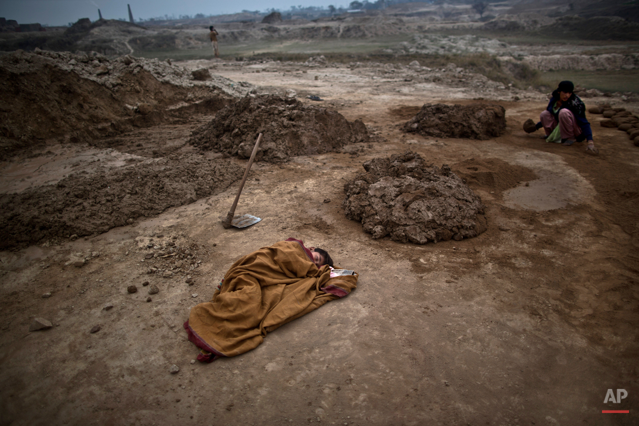  Pakistani boy, Adil Shahid, 6, suffering from a fever, sleeps on the ground wrapped with a shawl, next to his mother Najma, 25, at the site of her work in a brick factory in Mandra, near Rawalpindi, Pakistan, Monday, March 3, 2014. (AP Photo/Muhamme