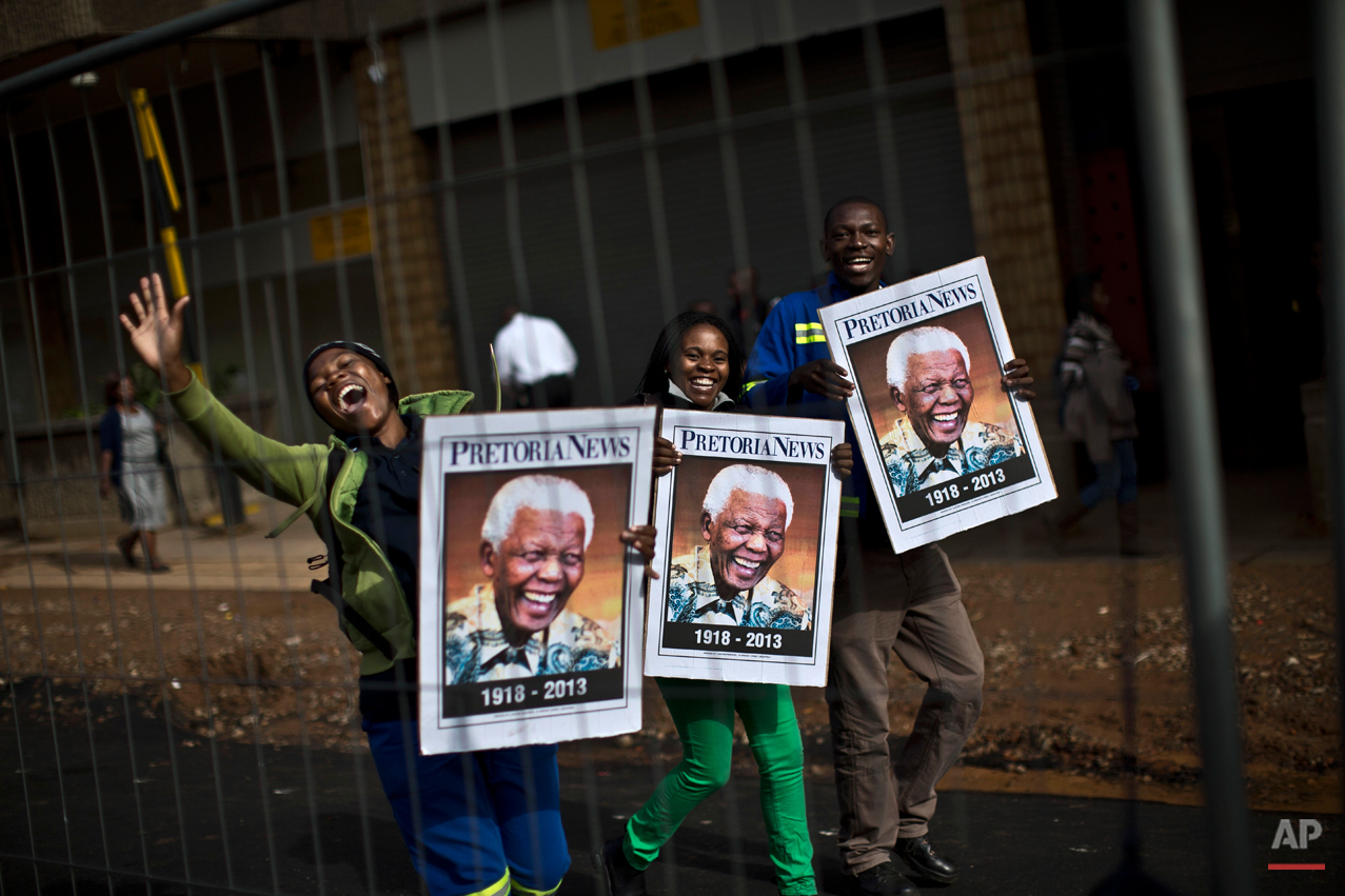  South African mourners hold posters of former president Nelson Mandela, while chanting slogans as the convoy transporting the body of Nelson Mandela passes by, in Pretoria, South Africa, Wednesday, Dec. 11, 2013. Motorcycle-riding police officers es