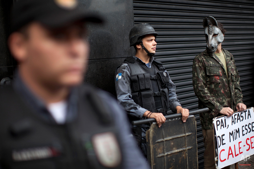  An activist wearing a donkey mask stands next to police as they stand guard outside a military club during a protest in downtown Rio de Janeiro, Brazil, Thursday March 29, 2012. A club of retired military officers held its annual celebration of Braz